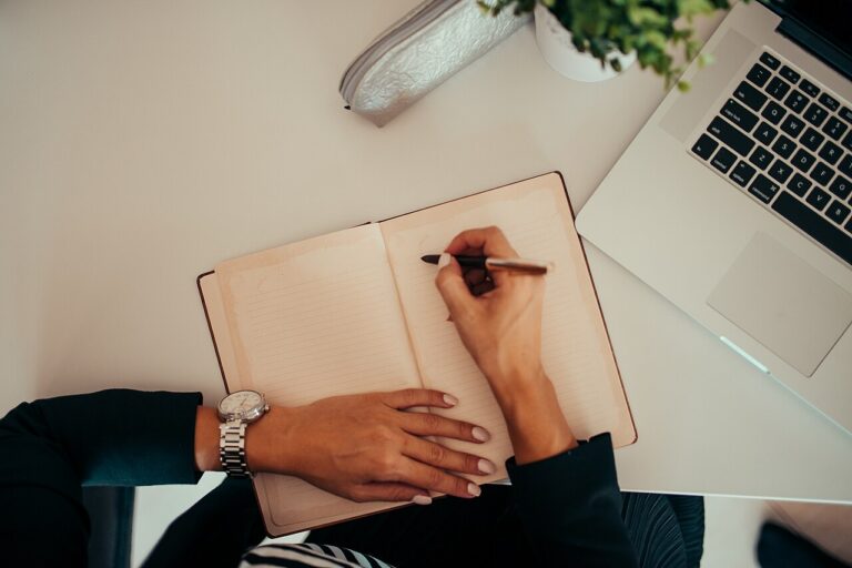 Exploring Nex777.com: What Users Should Know Before Getting Started Person researching at a modern workspace, writing notes beside a laptop